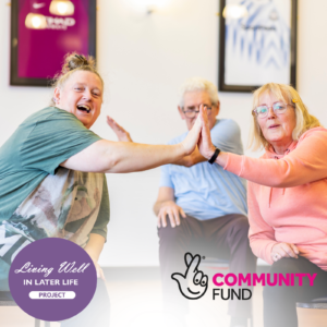 Image of three older people sat down doing high fives. They are happy and doing seated exercises. The National Lottery Community Fund logo is also in the image.