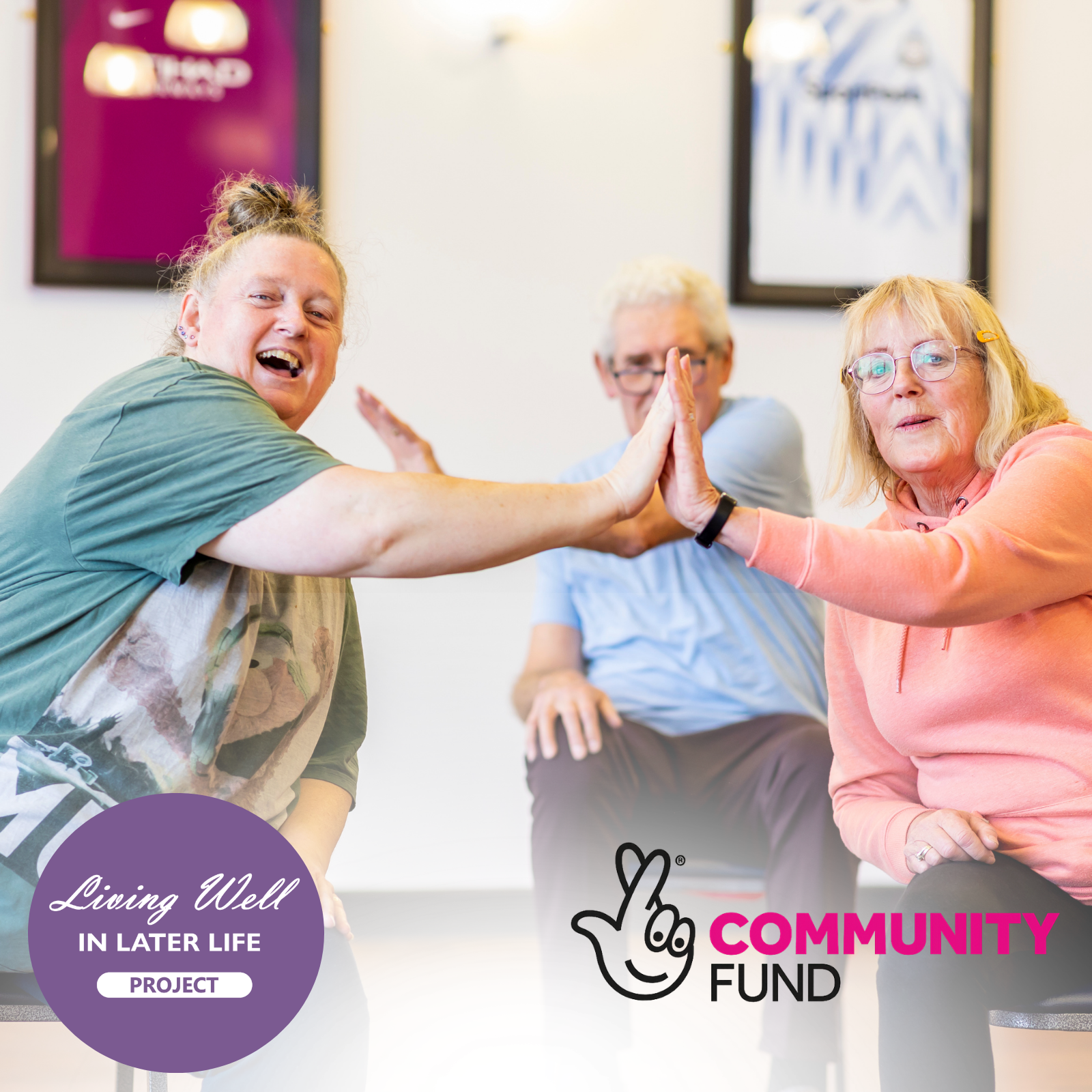 Image of three older people sat down doing high fives. They are happy and doing seated exercises. The National Lottery Community Fund logo is also in the image.
