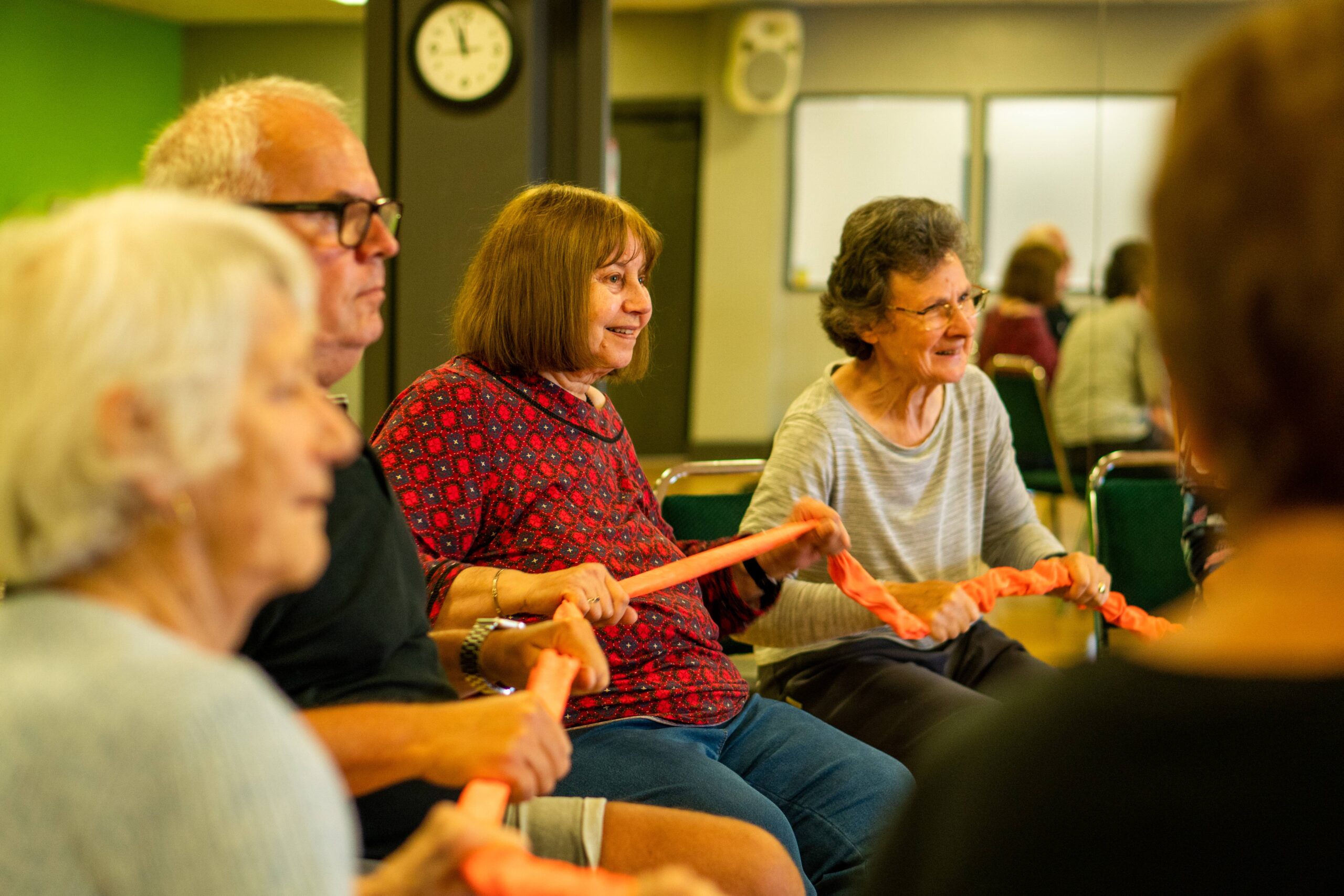 A group of older people sit in a circle on chair enjoying gentle seated movement exercises