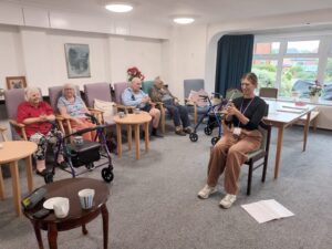 A group of older people sit in chairs following a female instructor with gentle seated exercise at age concern hampshire